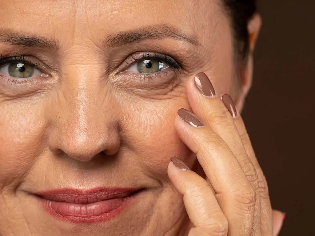 Mature woman gently touching visible fine lines and wrinkles around her eyes